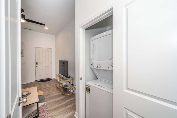 A laundry room with a front-loading washer and dryer, a small table with a basket, and a television on a stand. - Heart of Covington | 5-min Drive to Downtown Cincy (Covington)