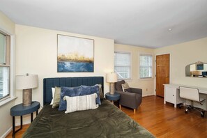 A bedroom with a bed, bedside lamps, a desk, a chair, and a painting on the wall.
