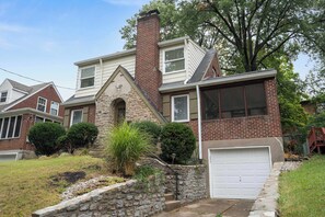 A two-story house with a brick chimney, a garage, and a stone wall.