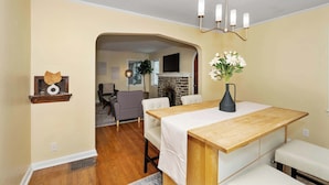 A dining area with a wooden table, white chairs, and a vase of flowers. There is a fireplace in the background and a ceiling light fixture above the table. - The Cincinnati Charm (Cincinnati)