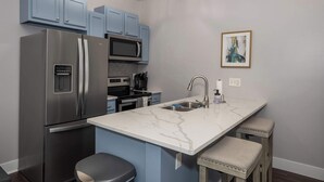 A modern kitchen with blue cabinets, stainless steel appliances, a marble countertop, and a sink. - Heart of Mainstrasse 2 (Covington)
