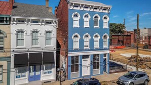 A two-story building with a blue facade and white trim, featuring large windows and a visible ground floor entrance. - Heart of Mainstrasse 2 (Covington)