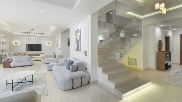 Un salon moderne avec un ensemble de canapés, un téléviseur à écran plat et un escalier menant à l’étage supérieur.