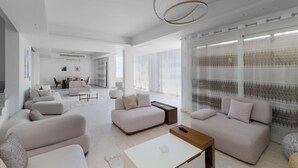 Un salon spacieux, doté d’un canapé moderne, d’une table basse et d’un coin repas à l’arrière-plan.