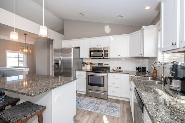 A modern kitchen with white cabinets, stainless steel appliances, granite countertops, and a built-in oven.