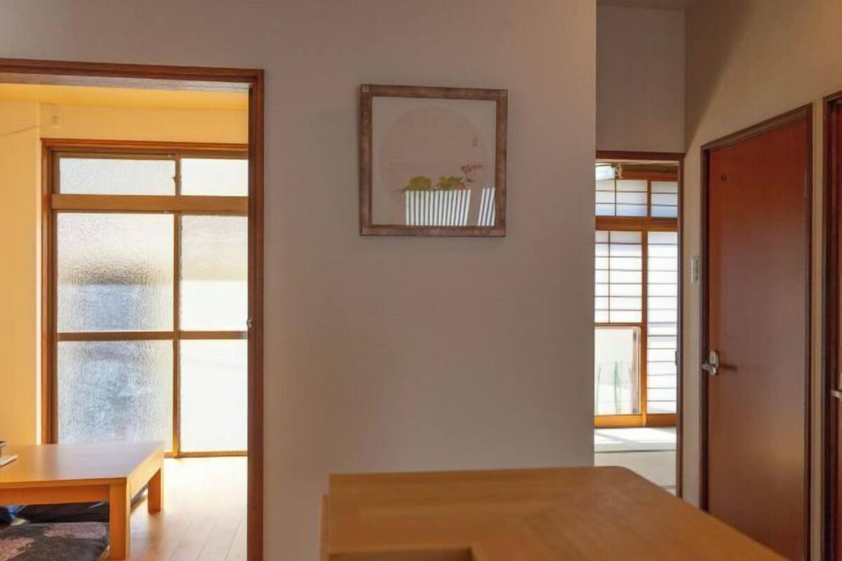 Een kamer met een houten tafel, een lijst met een afbeelding aan de muur en schuifdeuren die naar een andere ruimte leiden.