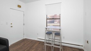 A room with a white door, a window with a view of buildings, a small table with two stools, and a ceiling-mounted light fixture. - Northside Suites 4 – Your Perfect Vacation Haven! (Cincinnati)