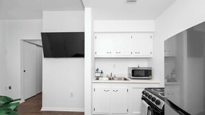 A compact kitchen with white cabinets, a microwave, a stove, and a flat-screen TV mounted on the wall. - Northside Suites 4 – Your Perfect Vacation Haven! (Cincinnati)