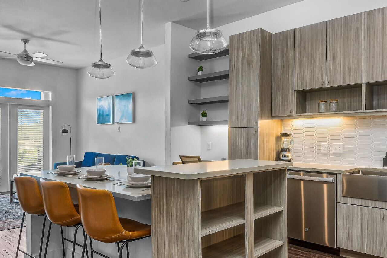 Eine moderne Küche mit Holzausbau, einer zentralen Kochinsel mit Barhocker, Pendelleuchten und einem integrierten Geschirrspüler.