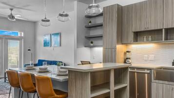 Una cocina moderna con armarios de madera, una isla central con taburetes de bar, iluminación colgante y un lavavajillas integrado.