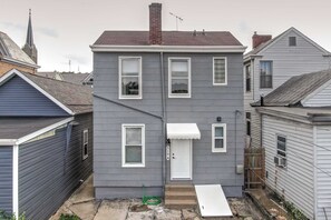 A two-story residential building with a grey exterior, white trim, and a small front porch.