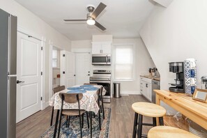 A compact kitchen with white cabinetry, a microwave, and a stove. There is a dining table with chairs and a small bar area with stools.