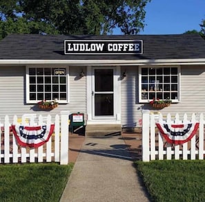 En café ved navn 'Ludlow Coffee' med et hvidt stakhegn, amerikanske flagudsmykninger og et skilt, der siger 'Gratis Vand'.