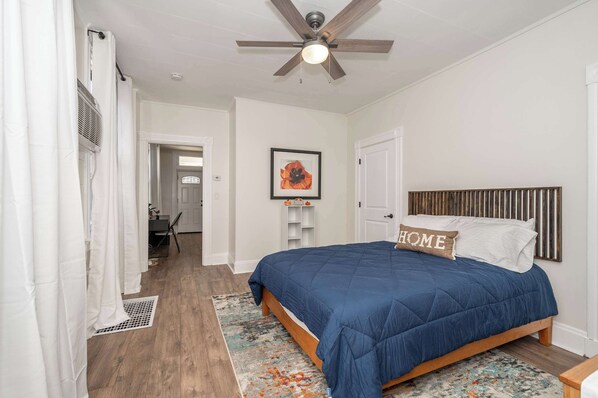 A bedroom with a bed, a ceiling fan, a framed picture, and a door.