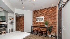 A modern kitchen with a marble countertop, a brick wall, and a hanging light fixture. - 2 King Beds | Near OTR + Downtown | Free Parking (Cincinnati)