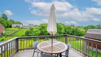 A wooden deck with a round table and chairs, an umbrella, and a view of a green landscape with houses in the background.