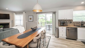 A modern kitchen with a wooden dining table, bar stools, a hanging light fixture, a dishwasher, and a view to an outdoor patio. - Poolside Paradise Near the Ark (Walton)