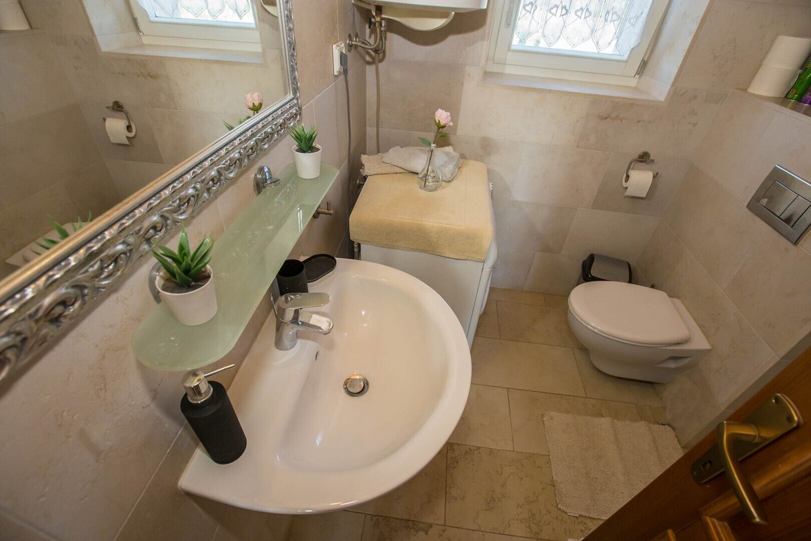 Et badeværelse med en hvid vask, et toilet og et spejl. To krukker med planter står på vaskeskabet.