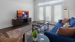 Ein modernes Wohnzimmer mit einem blauen Sofa, einer Unterhaltungseinheit aus dunklem Holz und einem großen Flachbildfernseher, der Streaming-Dienste anzeigt.