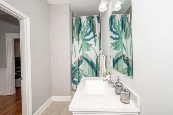 Un baño con lavamanos blanco, un espejo y una cortina de ducha con estampado de hojas.