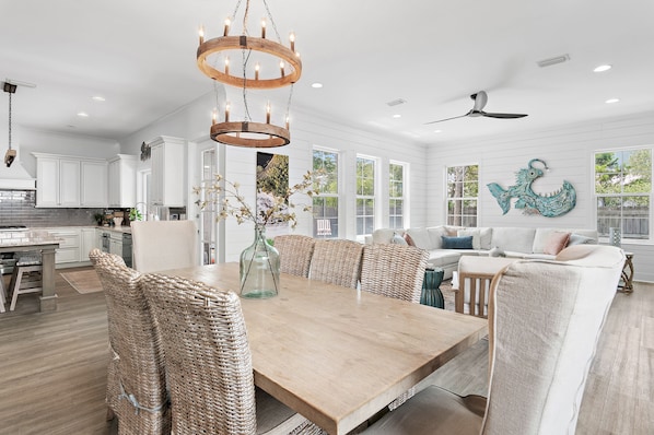 A spacious kitchen with white cabinets, a wooden dining table, wicker chairs, and a chandelier.
