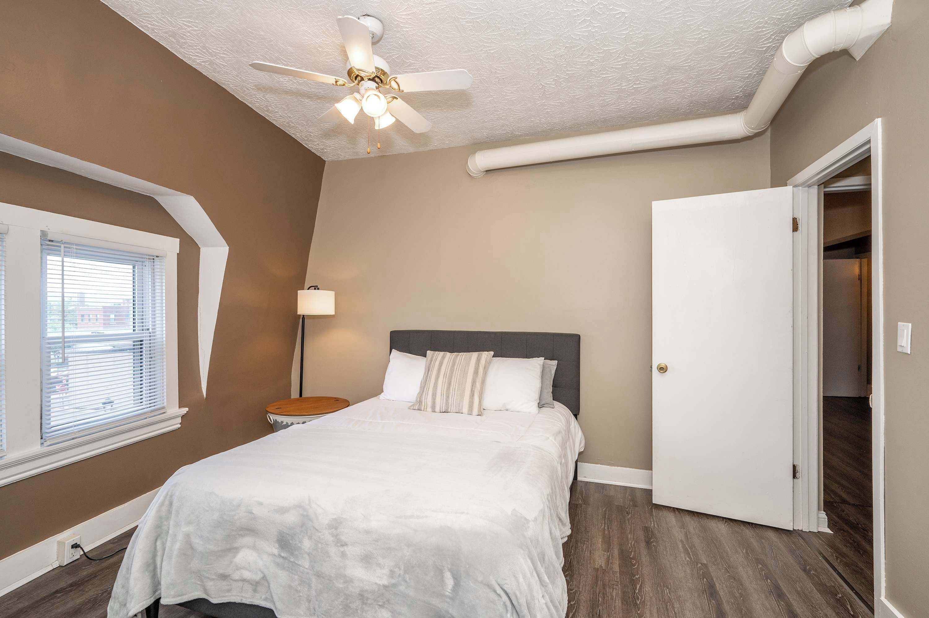 A bedroom with a bed, a ceiling fan, a nightstand, a lamp, and a door to another room.