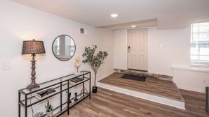A modern entryway with a wooden floor, a console table with books and a lamp, a mirror, and a potted plant. - Covington Charm 101 (Covington)