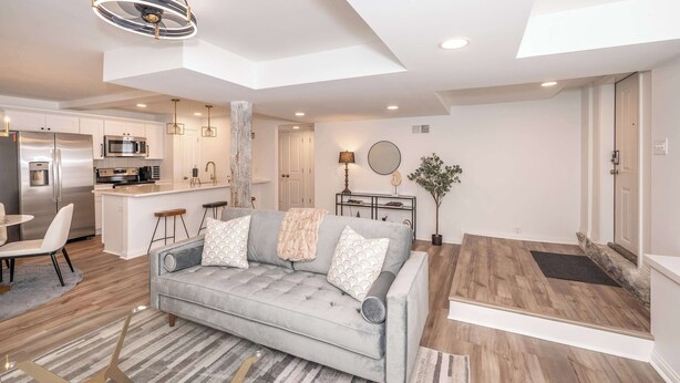 A modern living room with a grey sofa, a kitchen area with white cabinets, and a dining area with a table and chairs. - Covington Charm 101 (Covington)