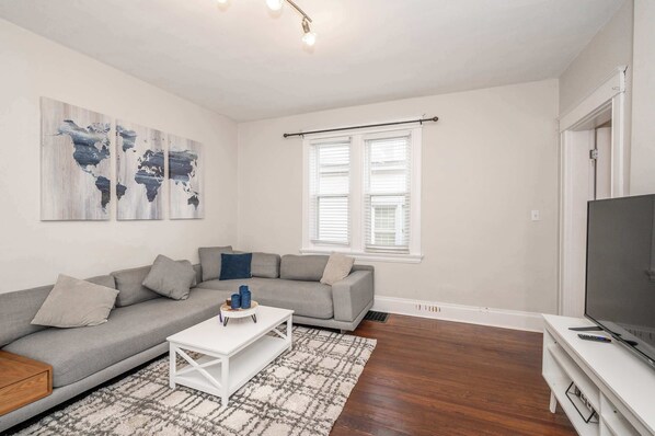 A living room with a grey sofa, white coffee table, and a TV on a stand.