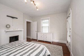 A bedroom with a bed, a fireplace, a dresser, a window, and a door.