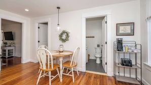 A dining area with a round table and four chairs, a hanging light fixture, and a doorway leading to a bathroom. - Historic Ludlow Apt B (Ludlow)