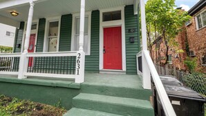 A green house with a red door, white porch railing, and steps leading to the front door. - Chic Modern Gem w/ Style Suites (Cincinnati)