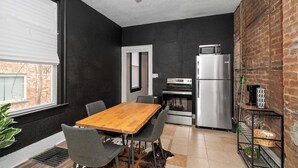 A compact kitchen with a wooden table and chairs, a refrigerator, and a microwave. - Chic Modern Gem w/ Style Suites (Cincinnati)