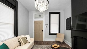 A living room with a beige sofa, a small armchair, a patterned rug, a fireplace, and a chandelier. - Chic Modern Gem w/ Style Suites (Cincinnati)