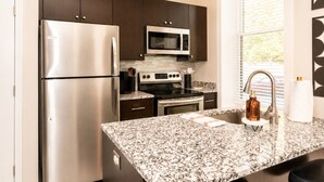 A modern kitchen with stainless steel appliances, dark cabinets, and a granite countertop. - OTR 1BR | Private Balcony | Near Downtown (Cincinnati)