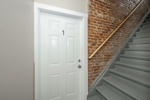 A white door with the number 1, a brick wall, and a grey staircase with a wooden handrail. - OTR 1BR | Private Balcony | Near Downtown (Cincinnati)