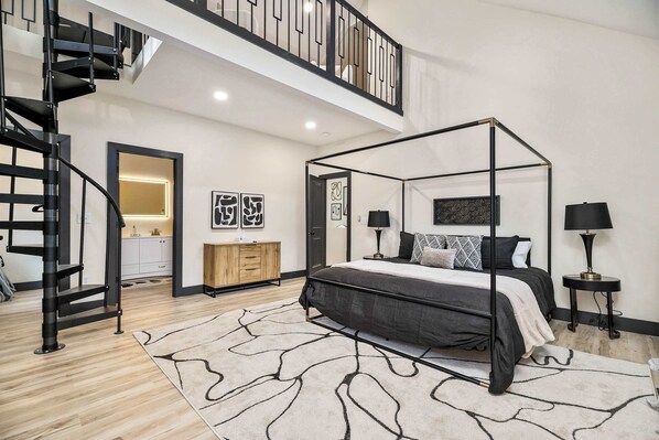 Une chambre moderne avec un lit à baldaquin, un escalier et une vue sur la cuisine et la salle de bain.