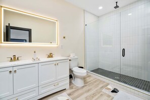 Une salle de bain moderne avec un meuble-lavabo blanc, des toilettes, une douche à parois de verre et un grand miroir doté d’un éclairage sous le meuble.