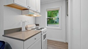 A compact kitchen with white cabinets, a stove, and a window providing a view of the outdoors.