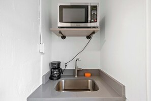 Una kitchenette compacta con microondas, cafetera y pileta.