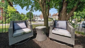 Two wicker sofas with cushions, a round wicker table, and a tree in a fenced outdoor area.