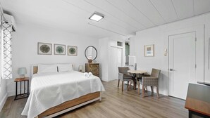 Un dormitorio con cama, mesitas de noche, cómoda, silla, mesita pequeña y una puerta.