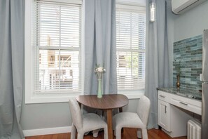 Een eethoek met een tafel en twee stoelen, een vaas met bloemen, en een keuken met een betegelde spatwand.