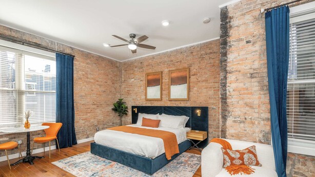 A bedroom with a brick wall, a bed, a desk, and a chair. - Findlay Market Suite 3 – For 2! (Cincinnati)
