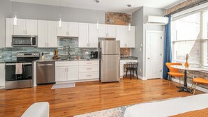 A modern kitchen with white cabinets, stainless steel appliances, and a brick accent wall. - Findlay Market Suite 3 – For 2! (Cincinnati)