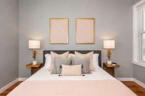 A bedroom with a bed, two bedside tables, lamps, and two framed wall art pieces.