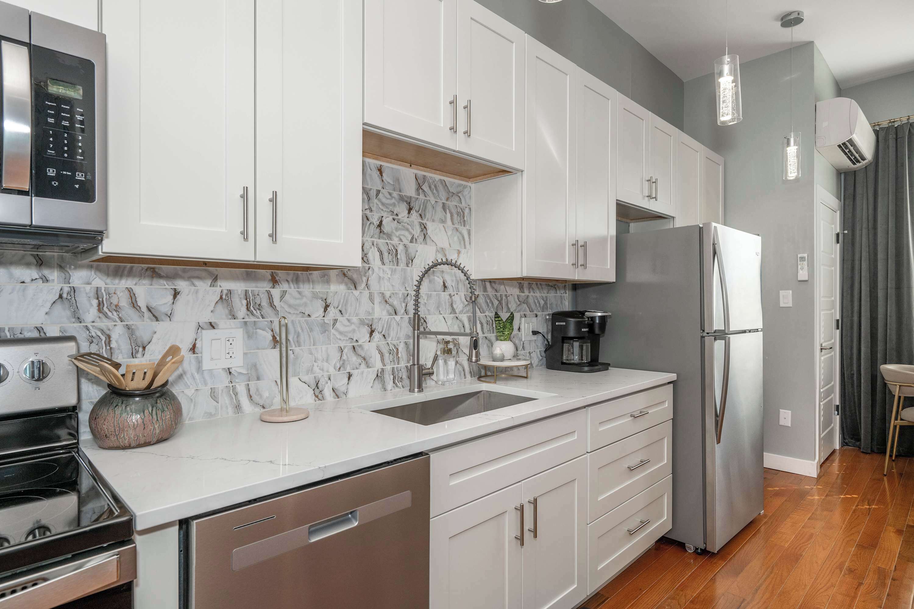 A modern kitchen with white cabinets, a marble backsplash, stainless steel appliances, and a wooden floor.