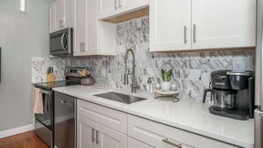 A modern kitchen with white cabinets, a stainless steel refrigerator, a built-in oven, a double sink, and a Keurig coffee maker. - Findlay Market Suite 5 – For 2! (Cincinnati)
