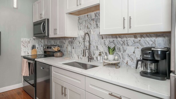 A modern kitchen with white cabinets, a stainless steel refrigerator, a built-in oven, a double sink, and a Keurig coffee maker. - Findlay Market Suite 5 – For 2! (Cincinnati)