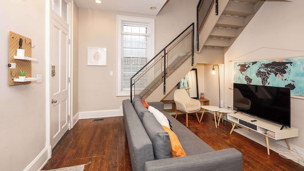 Un salon moderne avec un canapé gris, un téléviseur à écran plat, une carte du monde accrochée au mur et un escalier.